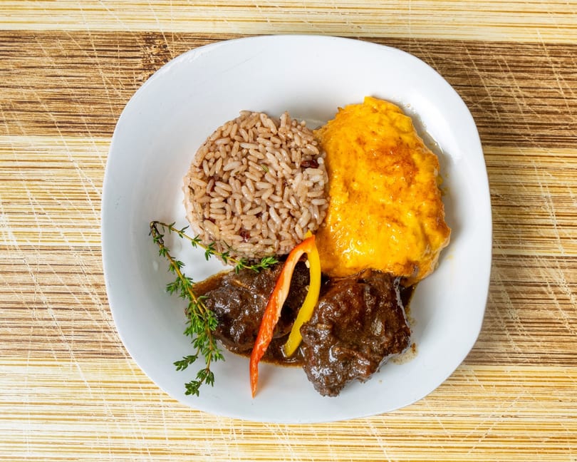 A white plate with brown rice, yellow mashed sweet potatoes, and stewed meat with thyme.