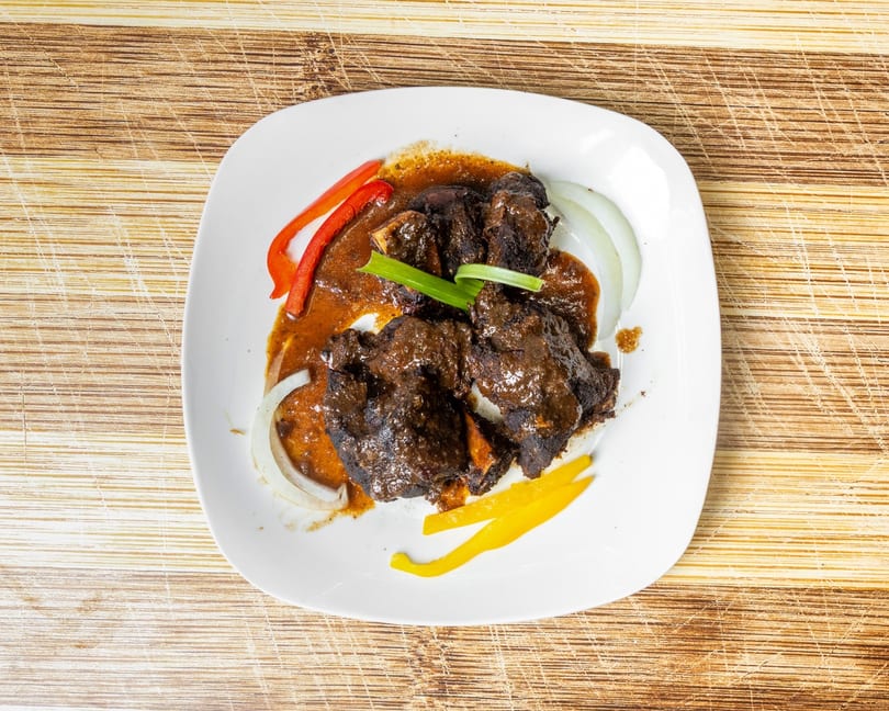 Braised oxtail in gravy with sliced red and yellow bell peppers, and white onions.
